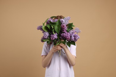 Photo of Teenage girl hiding behind bouquet of lilac flowers on beige background