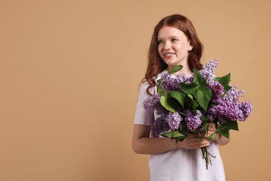 Photo of Smiling teenage girl with bouquet of lilac flowers on beige background. Space for text