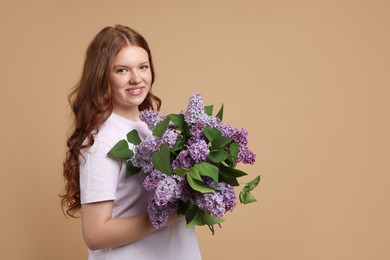 Photo of Smiling teenage girl with bouquet of lilac flowers on beige background. Space for text