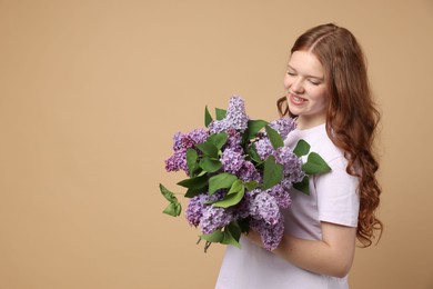 Photo of Smiling teenage girl with bouquet of lilac flowers on beige background. Space for text