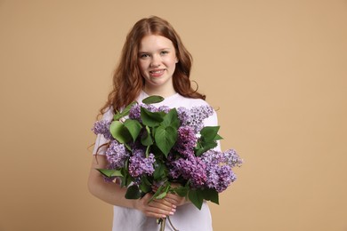 Photo of Smiling teenage girl with bouquet of lilac flowers on beige background