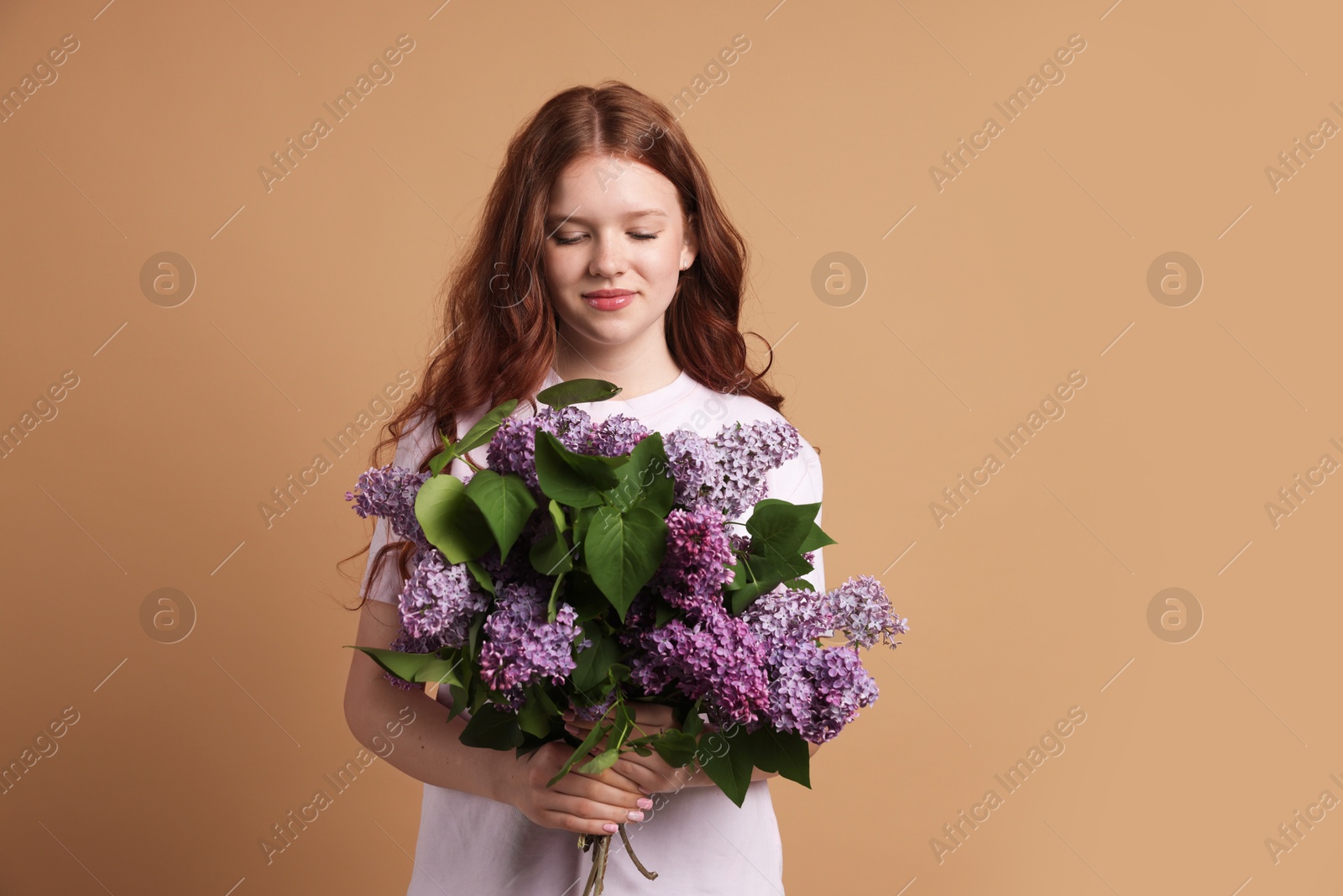 Beautiful teenage girl with bouquet of lilac flowers on beige background Photo of Beautiful teenage girl with bouquet of lilac flowers on beige background