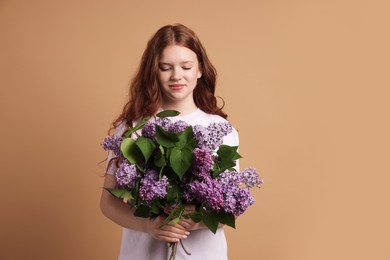 Photo of Beautiful teenage girl with bouquet of lilac flowers on beige background