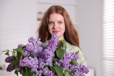 Photo of Portrait of beautiful teenage girl with lilac flowers at home