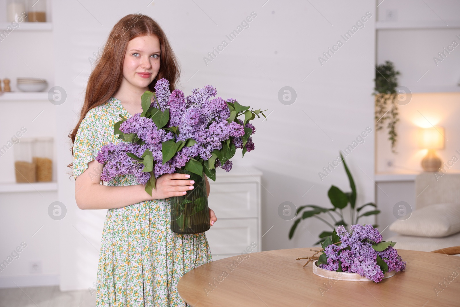Beautiful teenage girl holding vase with lilac flowers at home Photo of Beautiful teenage girl holding vase with lilac flowers at home