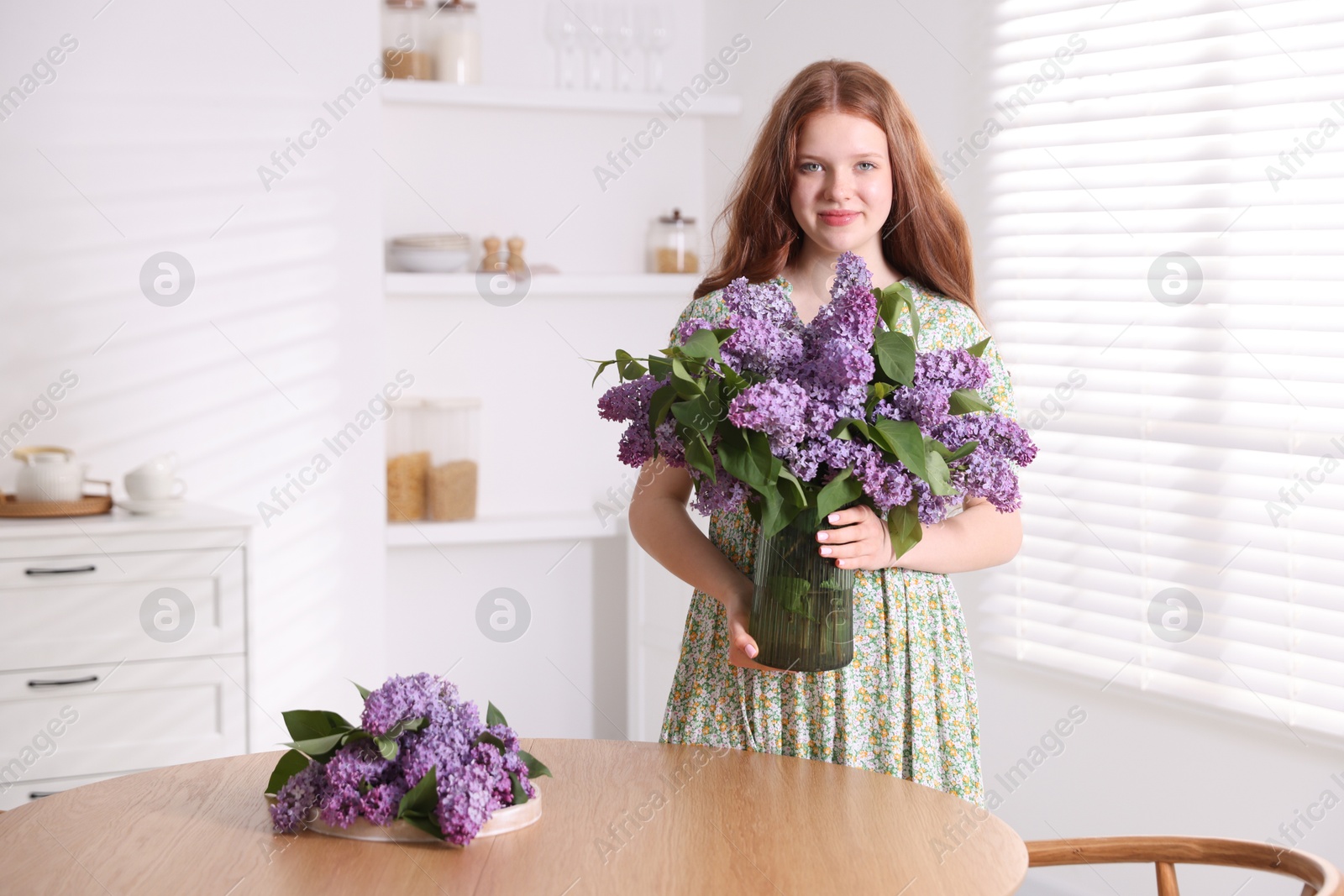 Beautiful teenage girl holding vase with lilac flowers at home Photo of Beautiful teenage girl holding vase with lilac flowers at home