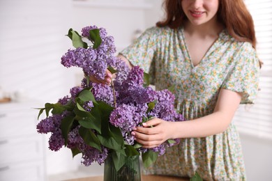 Photo of Smiling teenage girl putting branch with lilac flowers into vase at home, closeup