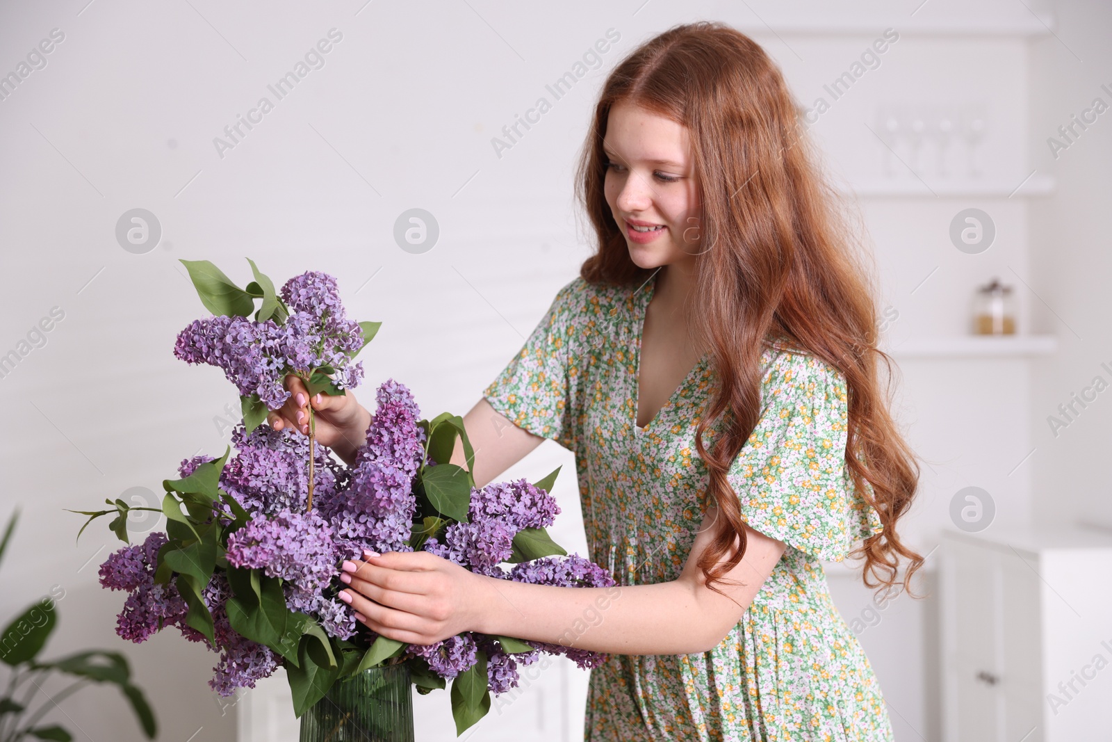 Smiling teenage girl putting branch with lilac flowers into vase at home Photo of Smiling teenage girl putting branch with lilac flowers into vase at home