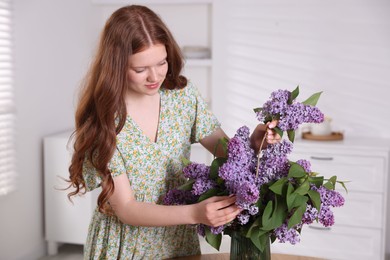 Photo of Beautiful teenage girl putting branch with lilac flowers into vase at home