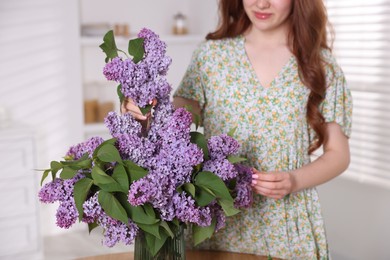 Photo of Teenage girl putting branch with lilac flowers into vase at home, closeup