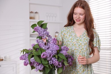 Photo of Smiling teenage girl putting branch with lilac flowers into vase at home