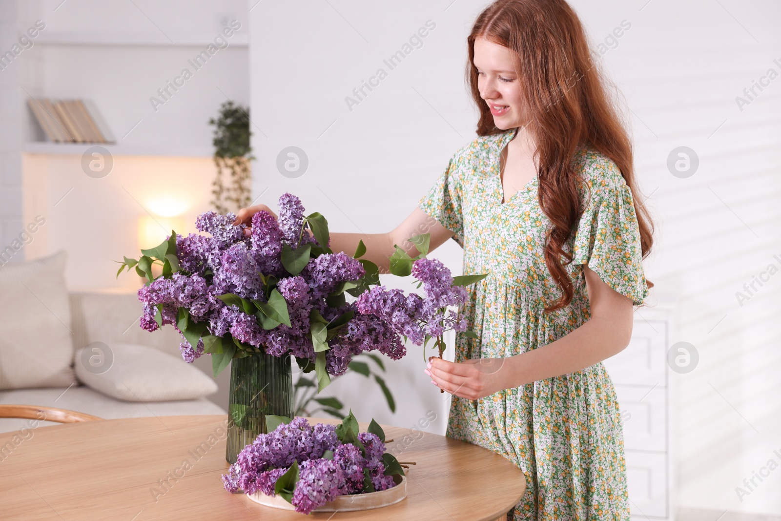 Smiling teenage girl with lilac flowers at table indoors Photo of Smiling teenage girl with lilac flowers at table indoors