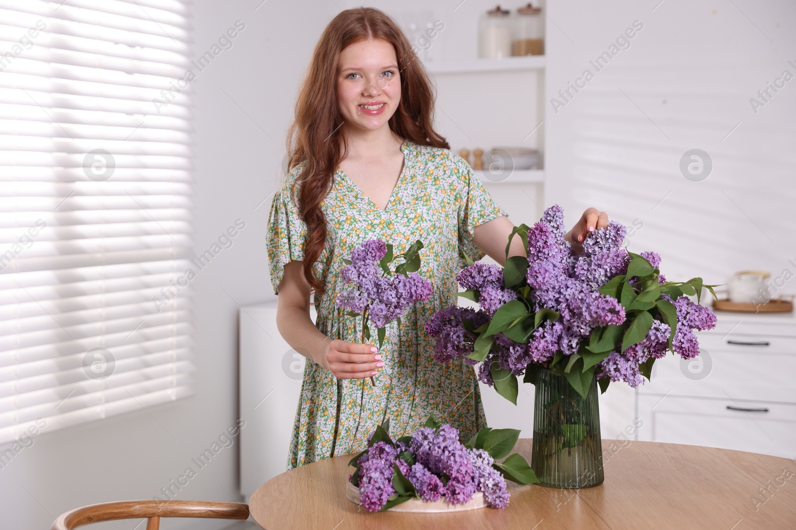 Smiling teenage girl with lilac flowers at table indoors Photo of Smiling teenage girl with lilac flowers at table indoors