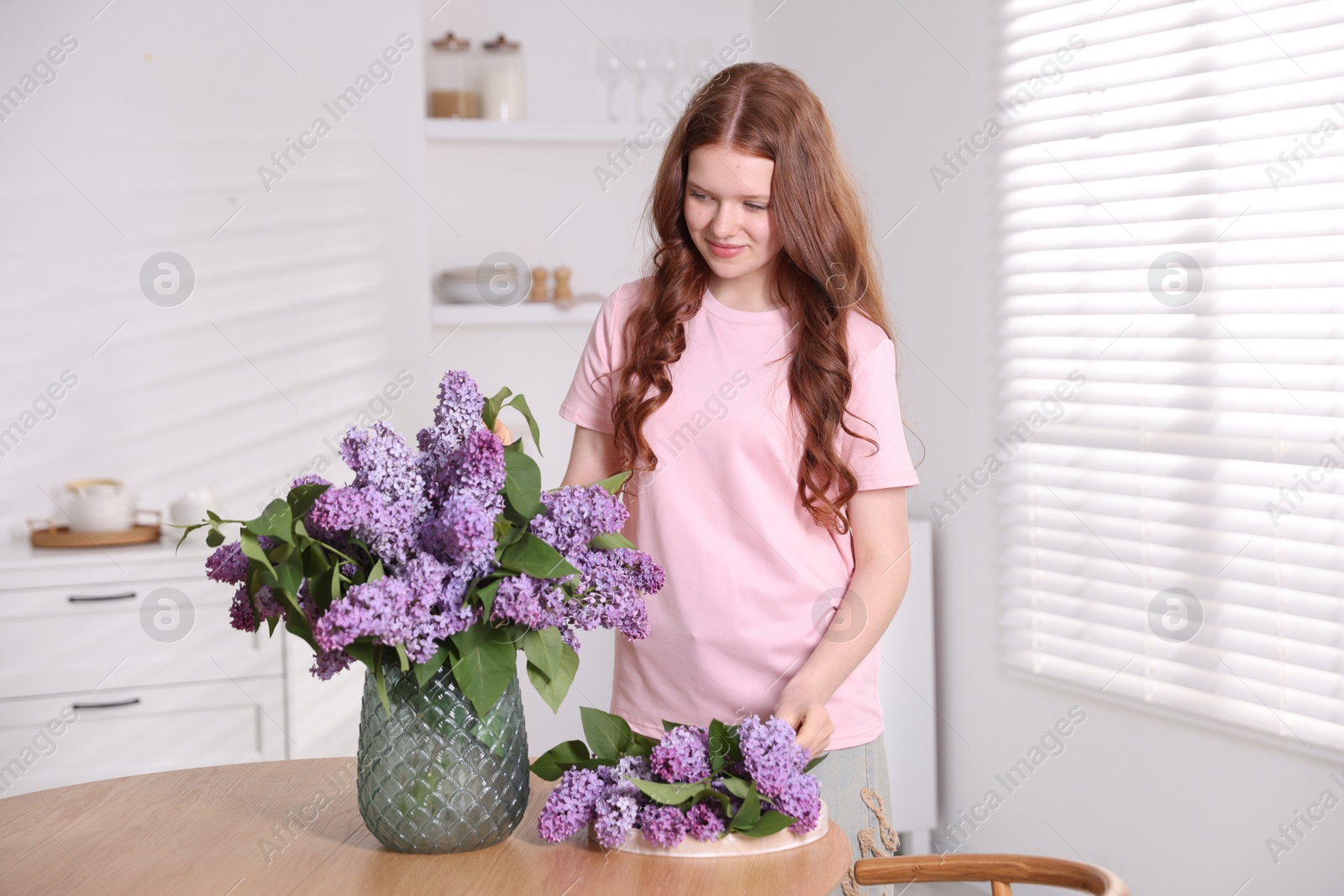 Beautiful teenage girl with lilac flowers at table indoors Photo of Beautiful teenage girl with lilac flowers at table indoors