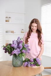 Photo of Smiling teenage girl with lilac flowers at table indoors