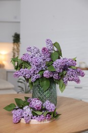 Photo of Branches with beautiful lilac flowers on wooden table indoors