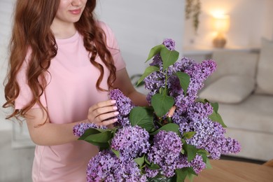 Photo of Teenage girl putting branch with lilac flowers into vase at home, closeup