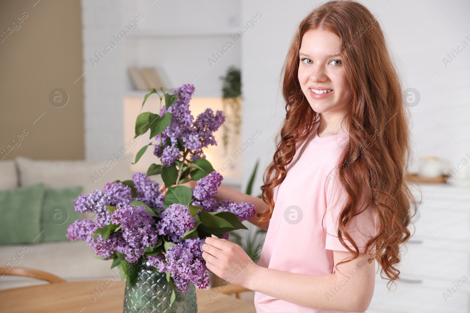 Smiling teenage girl putting branch with lilac flowers into vase at home Photo of Smiling teenage girl putting branch with lilac flowers into vase at home