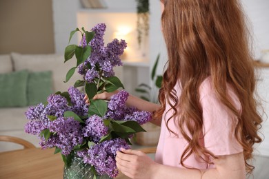 Photo of Teenage girl putting branch with lilac flowers into vase at home