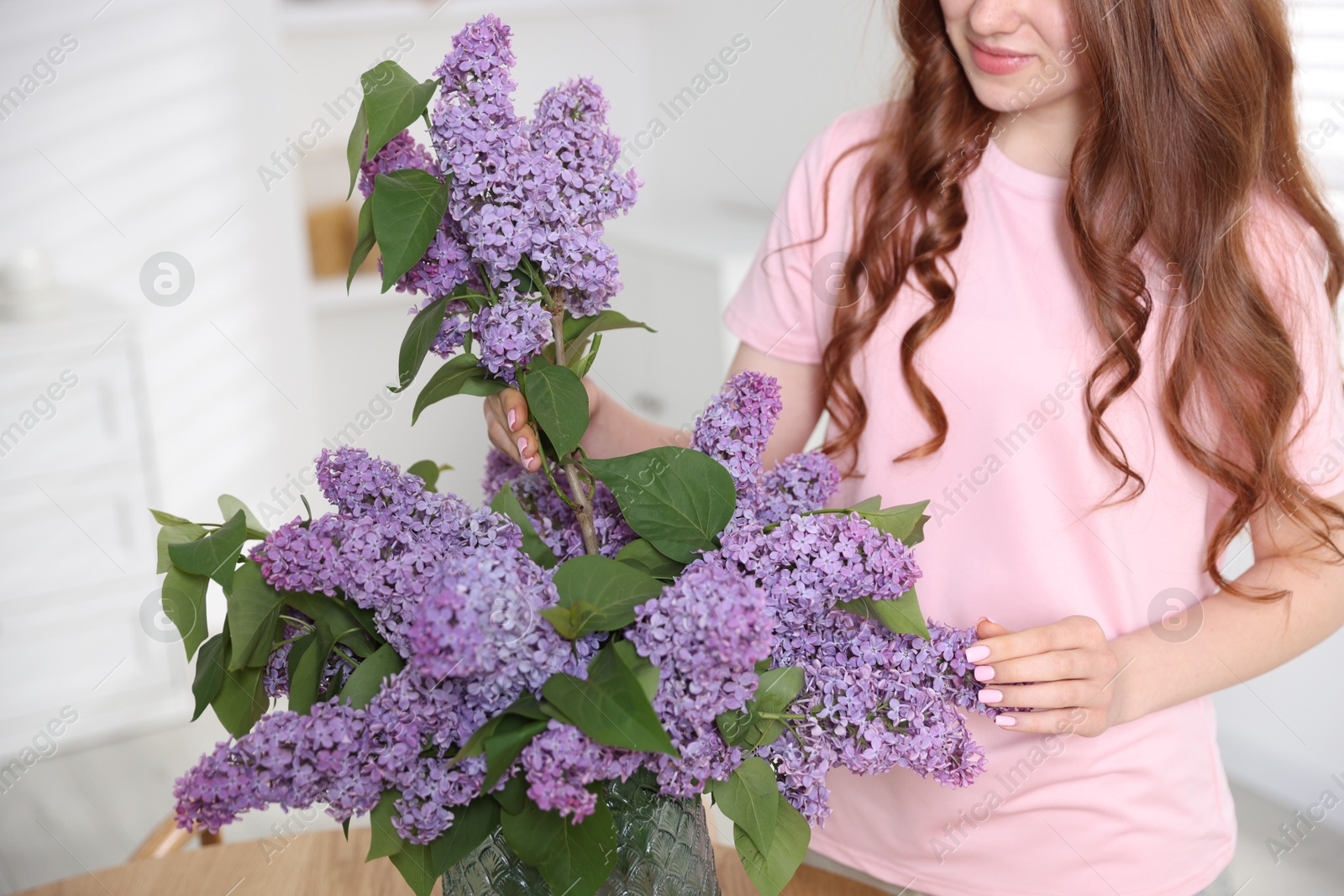 Teenage girl putting branch with lilac flowers into vase at home, closeup Photo of Teenage girl putting branch with lilac flowers into vase at home, closeup