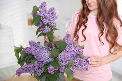 Photo of Teenage girl putting branch with lilac flowers into vase at home, closeup