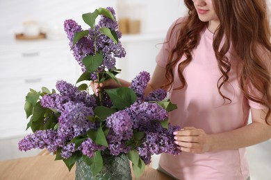 Photo of Teenage girl putting branch with lilac flowers into vase at home, closeup