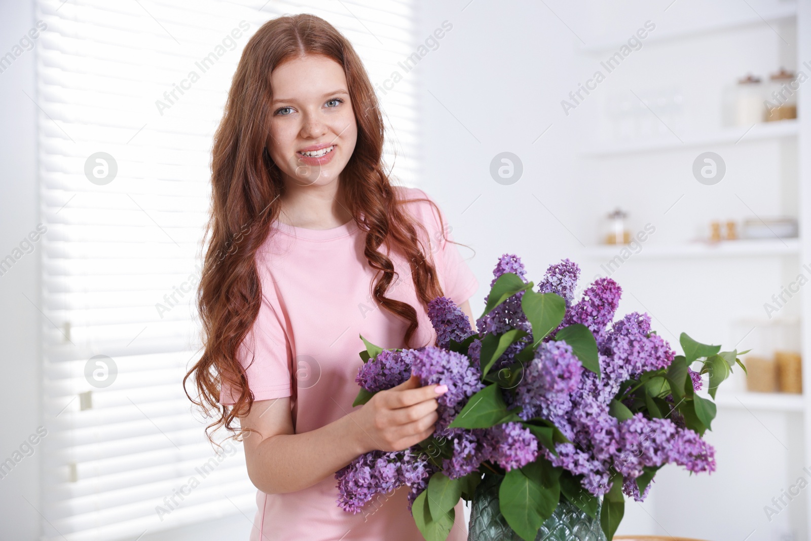 Smiling teenage girl with lilac flowers at home Photo of Smiling teenage girl with lilac flowers at home