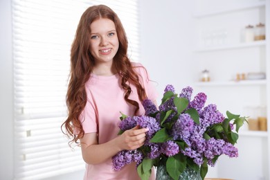 Photo of Smiling teenage girl with lilac flowers at home
