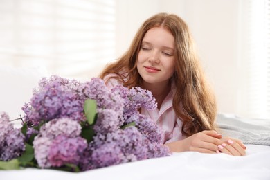 Photo of Beautiful teenage girl with bouquet of lilac flowers on bed indoors