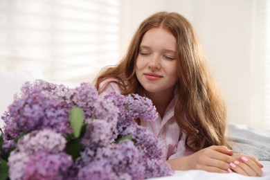 Photo of Beautiful teenage girl with bouquet of lilac flowers on bed indoors