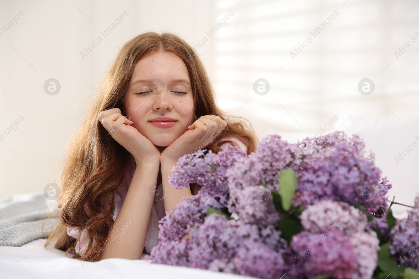 Beautiful teenage girl with bouquet of lilac flowers on bed indoors Photo of Beautiful teenage girl with bouquet of lilac flowers on bed indoors