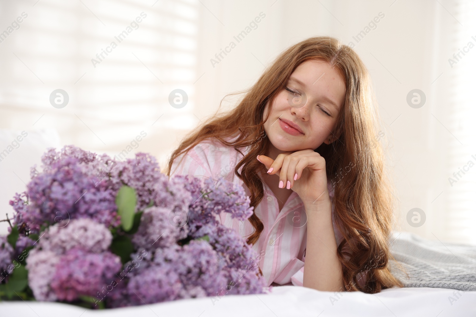 Beautiful teenage girl with bouquet of lilac flowers on bed indoors Photo of Beautiful teenage girl with bouquet of lilac flowers on bed indoors