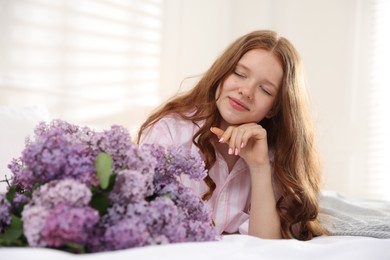 Photo of Beautiful teenage girl with bouquet of lilac flowers on bed indoors