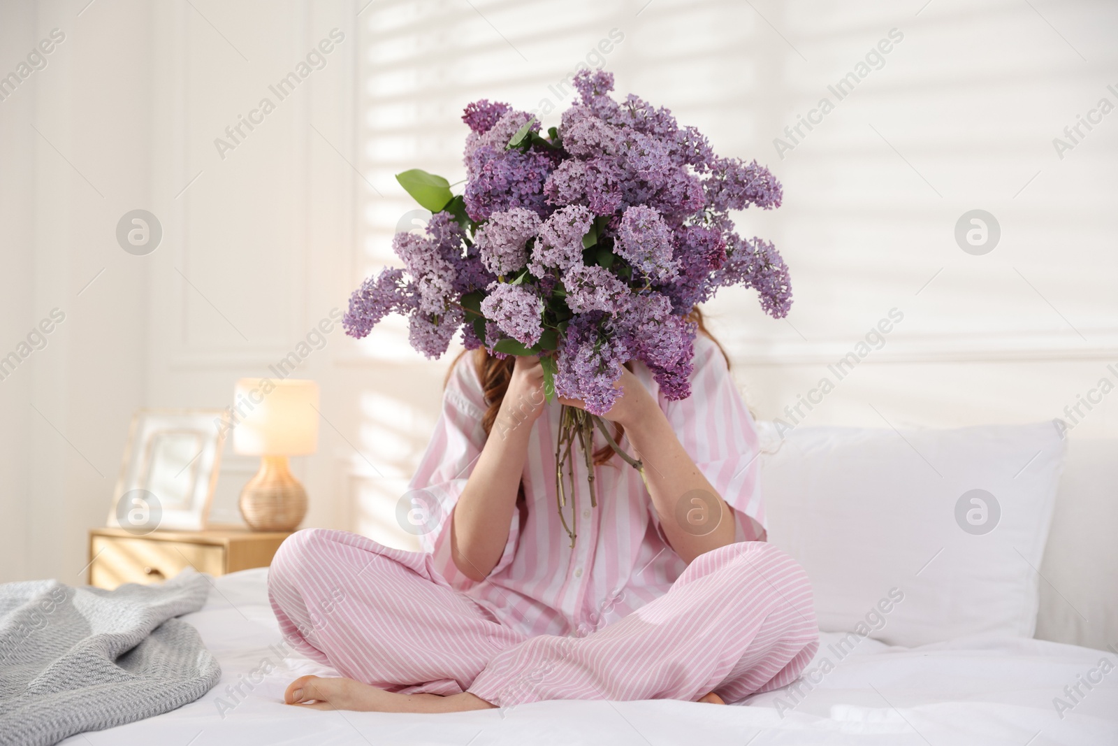 Teenage girl hiding behind bouquet of lilac flowers on bed at home Photo of Teenage girl hiding behind bouquet of lilac flowers on bed at home