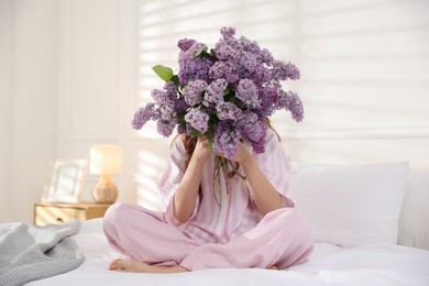 Photo of Teenage girl hiding behind bouquet of lilac flowers on bed at home