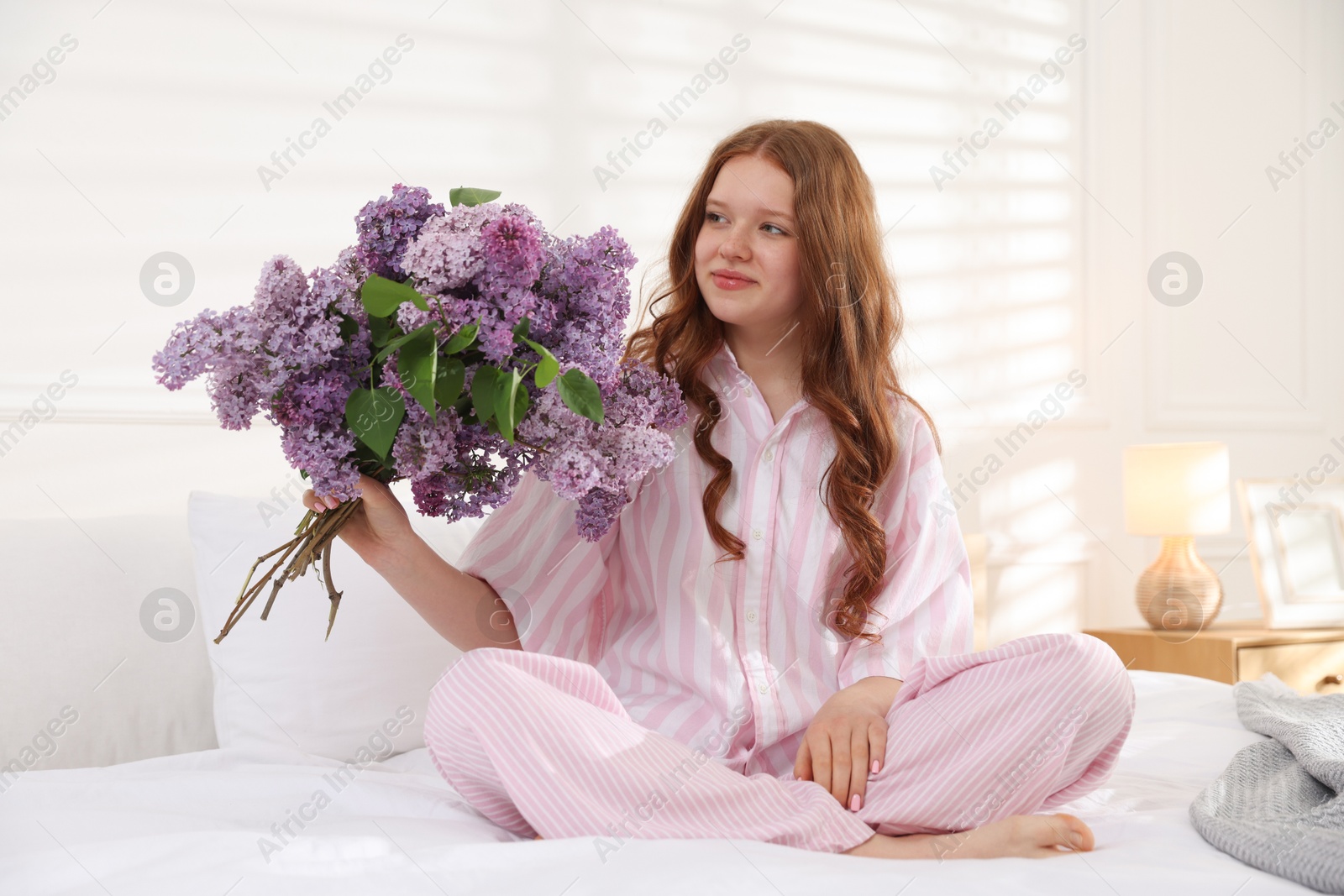 Beautiful teenage girl with bouquet of lilac flowers on bed indoors Photo of Beautiful teenage girl with bouquet of lilac flowers on bed indoors