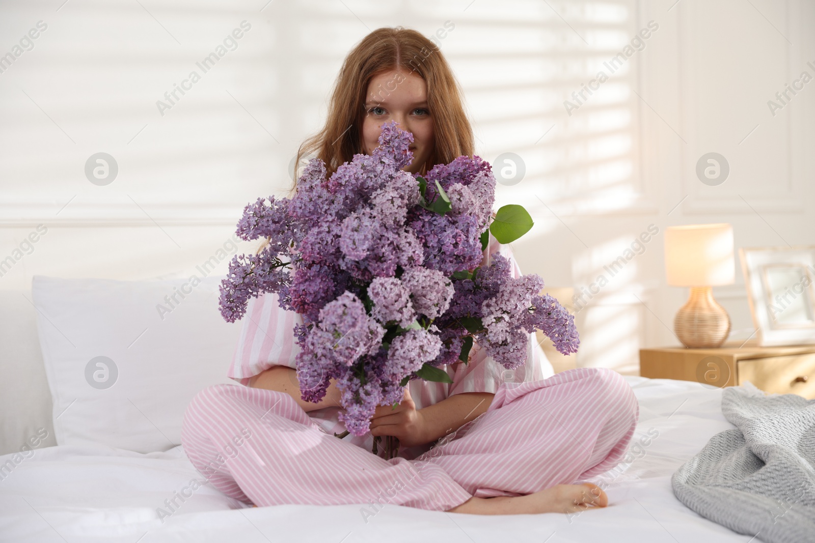 Beautiful teenage girl with bouquet of lilac flowers on bed indoors Photo of Beautiful teenage girl with bouquet of lilac flowers on bed indoors