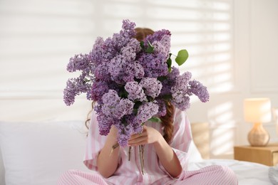 Photo of Teenage girl hiding behind bouquet of lilac flowers on bed at home