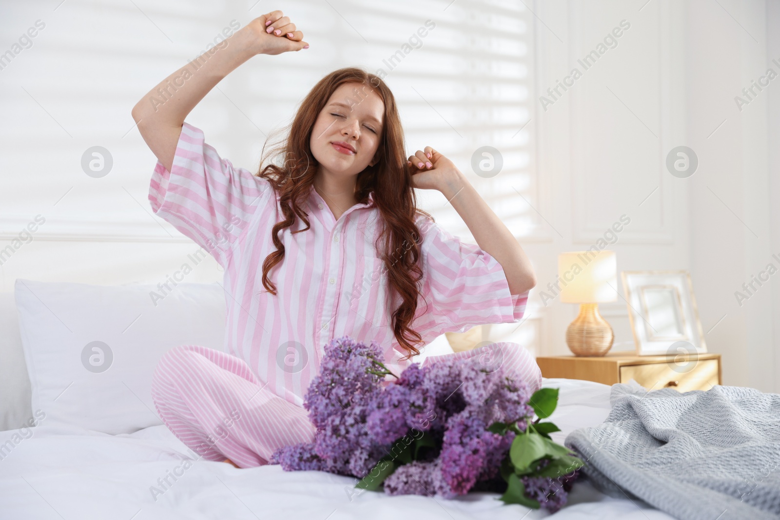 Beautiful teenage girl stretching near bouquet of lilac flowers on bed indoors Photo of Beautiful teenage girl stretching near bouquet of lilac flowers on bed indoors