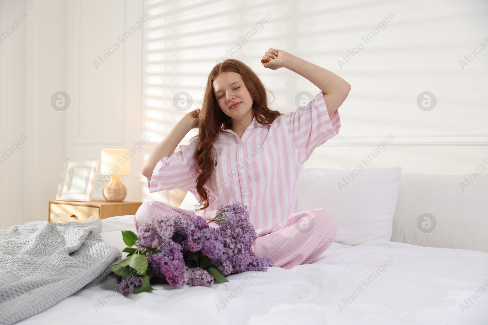 Beautiful teenage girl stretching near bouquet of lilac flowers on bed indoors Photo of Beautiful teenage girl stretching near bouquet of lilac flowers on bed indoors