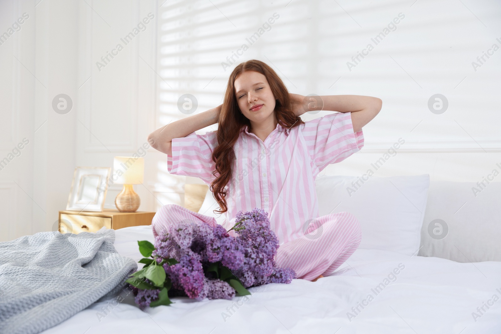 Beautiful teenage girl stretching near bouquet of lilac flowers on bed indoors Photo of Beautiful teenage girl stretching near bouquet of lilac flowers on bed indoors