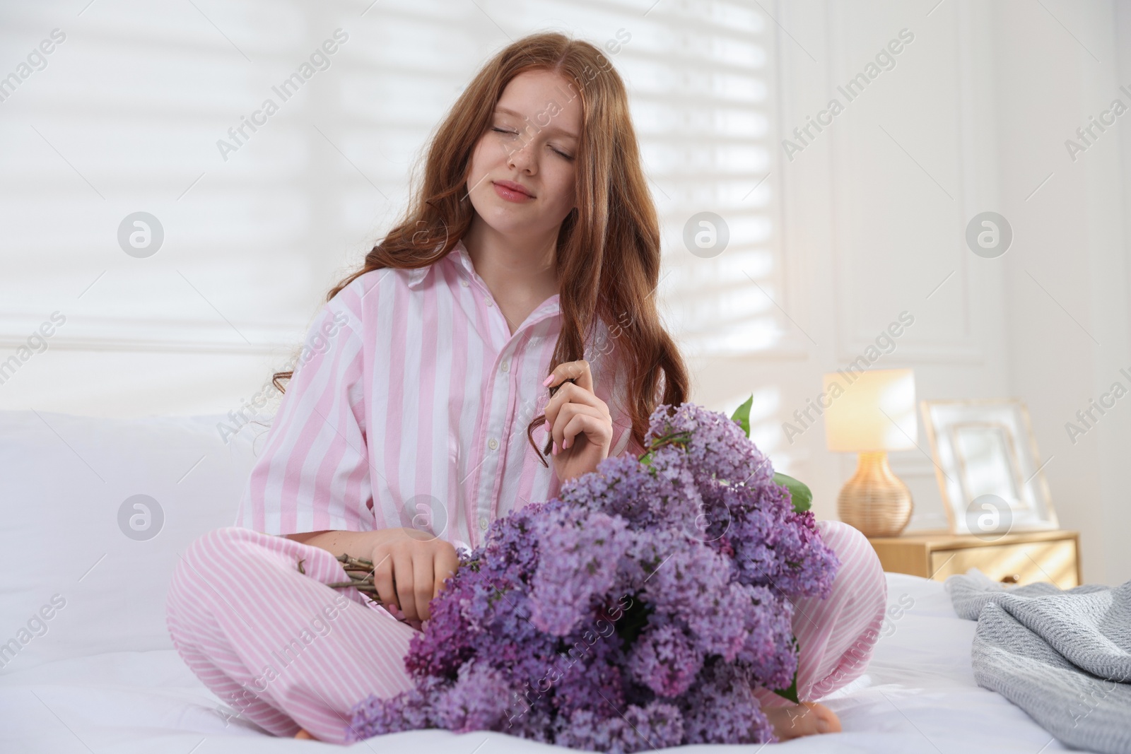 Beautiful teenage girl with bouquet of lilac flowers on bed indoors Photo of Beautiful teenage girl with bouquet of lilac flowers on bed indoors