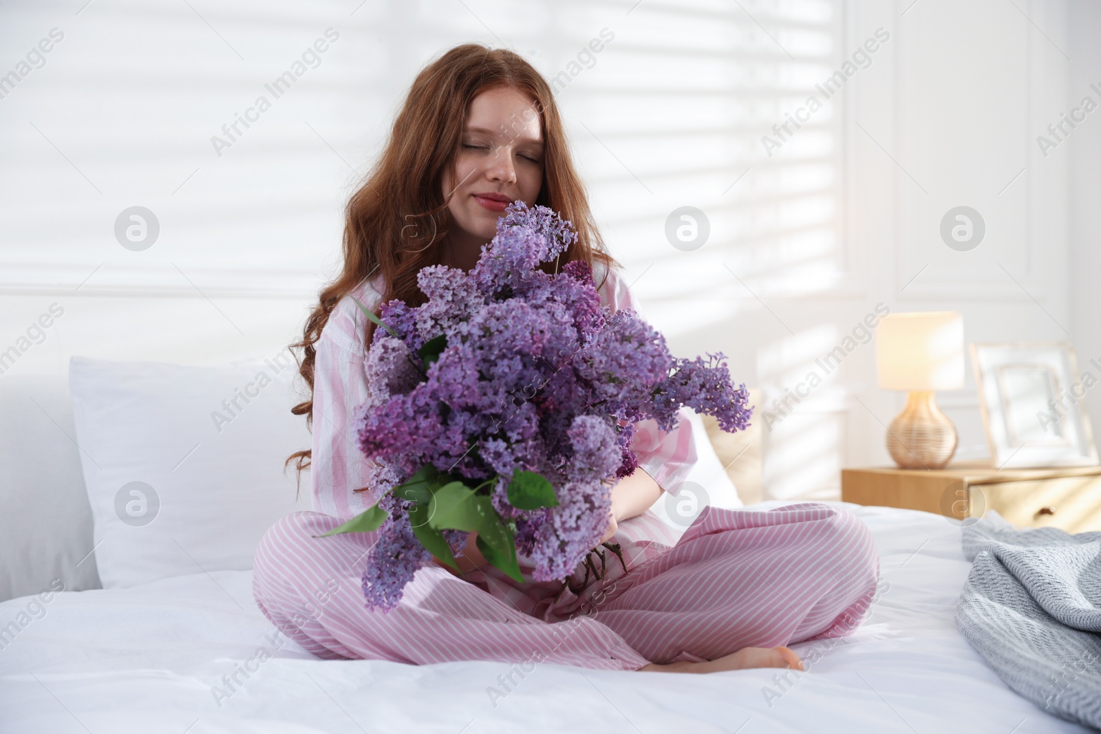Beautiful teenage girl with bouquet of lilac flowers on bed indoors Photo of Beautiful teenage girl with bouquet of lilac flowers on bed indoors