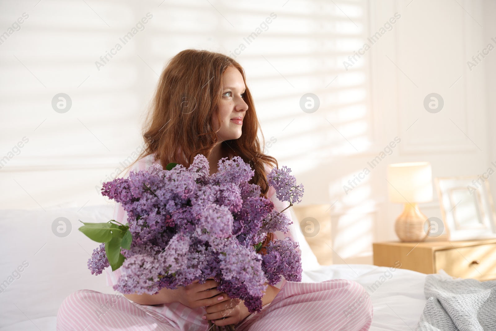 Beautiful teenage girl with bouquet of lilac flowers on bed indoors Photo of Beautiful teenage girl with bouquet of lilac flowers on bed indoors