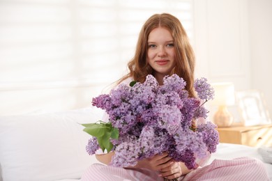 Photo of Beautiful teenage girl with bouquet of lilac flowers on bed indoors. Space for text
