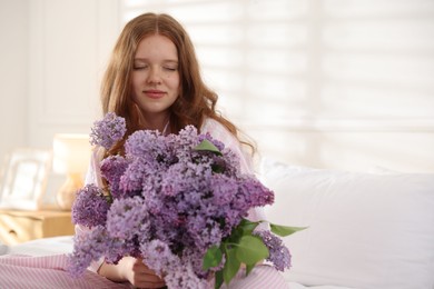 Photo of Beautiful teenage girl with bouquet of lilac flowers on bed indoors. Space for text