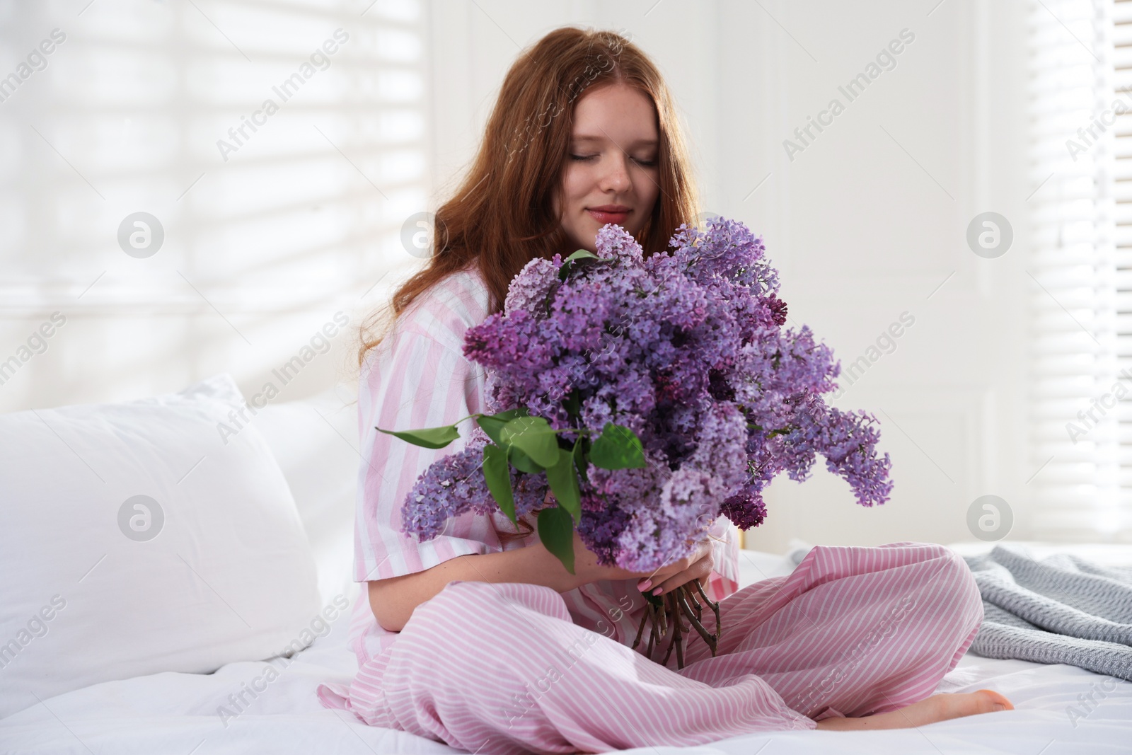 Beautiful teenage girl with bouquet of lilac flowers on bed indoors Photo of Beautiful teenage girl with bouquet of lilac flowers on bed indoors