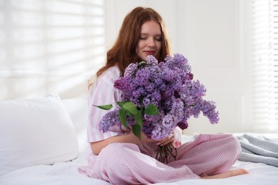 Photo of Beautiful teenage girl with bouquet of lilac flowers on bed indoors