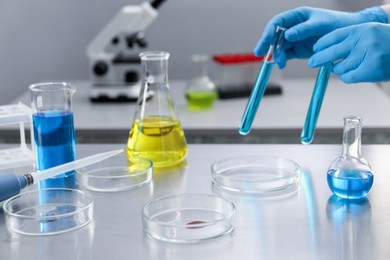 Photo of Scientist holding test tubes at table with Petri dishes in laboratory, closeup