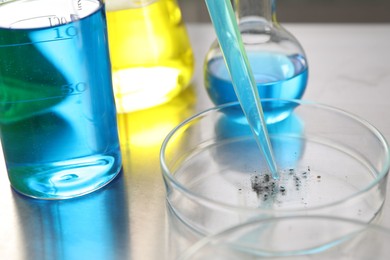 Photo of Dripping liquid from pipette into Petri dish at metal table, closeup